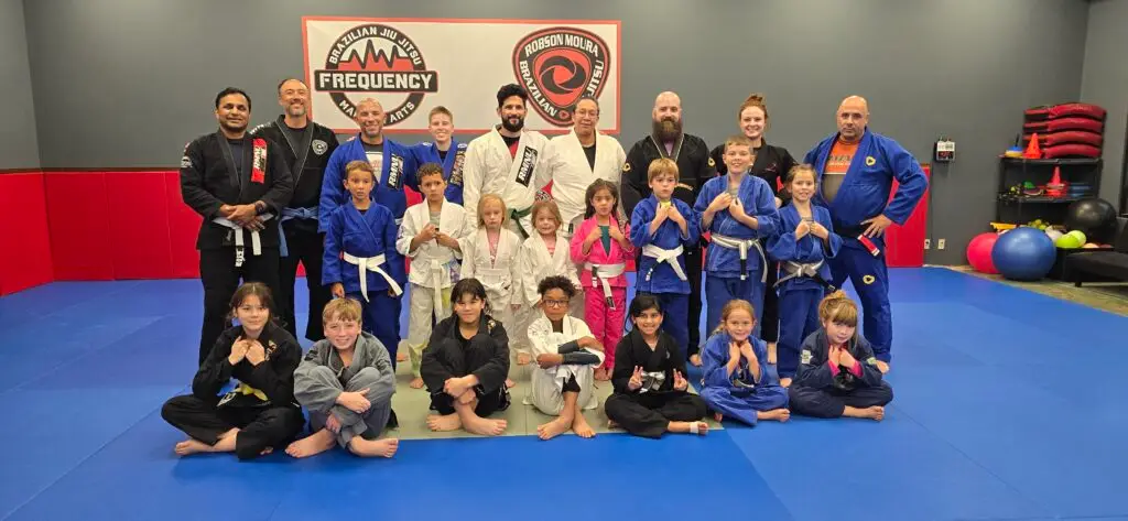 Youth Brazilian Jiu-Jitsu students and coaches posing for a group photo at Frequency Martial Arts in Bloomington, Illinois.