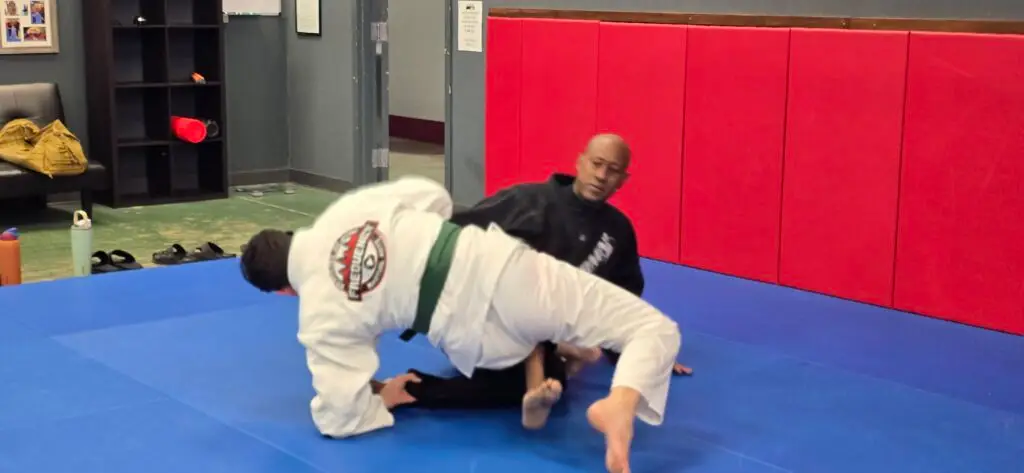 Two Brazilian Jiu-Jitsu practitioners demonstrating a ground technique on blue mats at Frequency Martial Arts in Bloomington, Illinois.